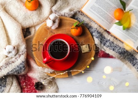Top view red coffee cup on wooden cut with winter essentials clementine mandarin, plaid, book and glowing christmas lights on the white wooden window sill. Christmas, holiday morning comfort concept