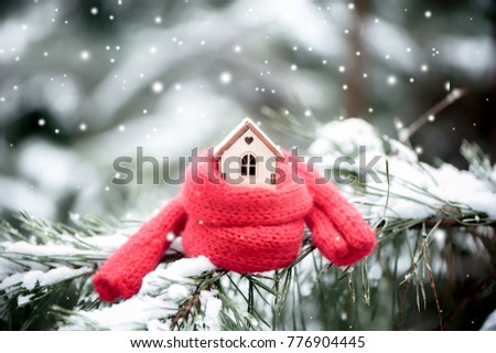 Christmas Toy house is wrapped in a warm scarf, it's snowing.on a natural natural background of a real fir in the snow, toned. Concept of winter, Christmas, new year,
 warm, cozy, loving, protecting t Royalty-Free Stock Photo #776904445