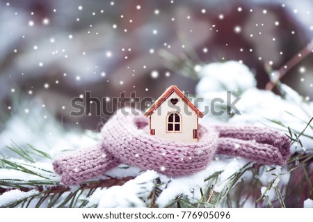 Christmas Toy house is wrapped in a warm scarf, it's snowing.on a natural natural background of a real fir in the snow, toned. Concept of winter, Christmas, new year,
 warm, cozy, loving, protecting  Royalty-Free Stock Photo #776905096
