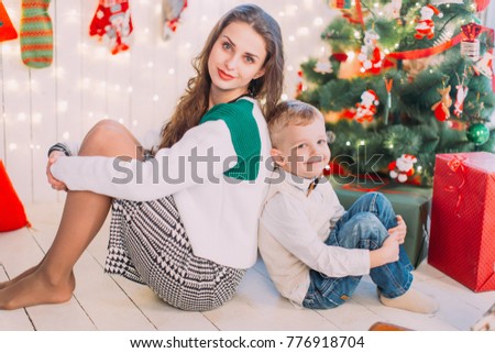 Winter holiday and celebration concept. New Year's picture of happy mother and child sitting on background of Christmas decorations