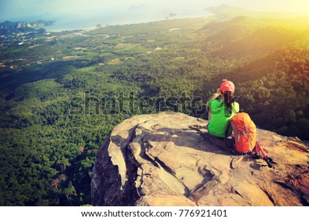 successful woman hiker taking picture with smartphone at cliff edge on mountain top
