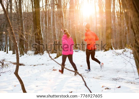 Young couple running away from the camera in a snow covered forest. Active and healthy lifestyle concept.