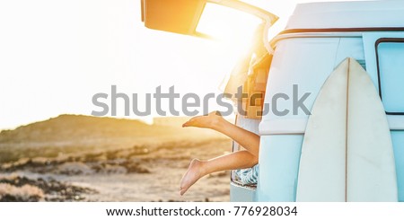 Legs view of happy surfer girl inside minivan at sunset - Young woman having fun on summer vacation - Travel,sport and nature concept - Focus on feet - Warm contrast filter Royalty-Free Stock Photo #776928034