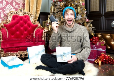 Macho smile with mobile phone at xmas tree. Man open present box with smartphone at Christmas tree. Winter holidays celebration. New year gift, surprise. Boxing day concept.