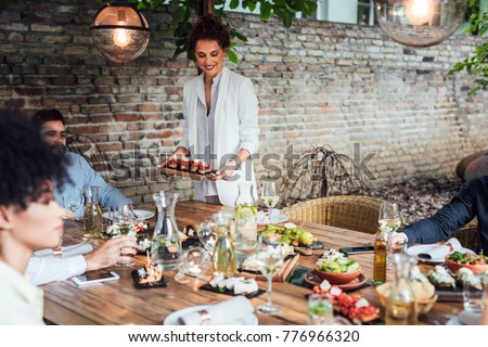 Pretty Caucasian smiling woman putting a plate with meal on dining table at backyard celebration.