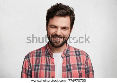 Pleased pleasant looking young student with beard and trendy hairdo wears casual checkered shirt, smiles pleasantly in camera, glad to pass session sucessfully, isolated over white background Royalty-Free Stock Photo #776970700