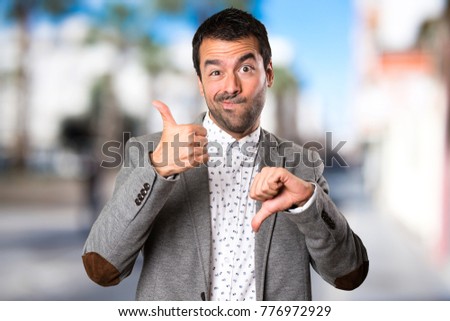 Handsome man making good-bad sign on unfocused background
