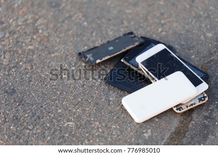 Several broken smartphones are on the asphalt.