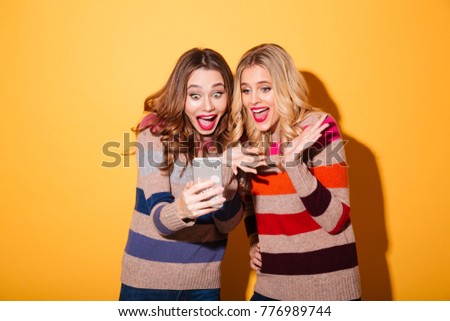Portrait of two happy girls standing with mobile phone isolated over white background