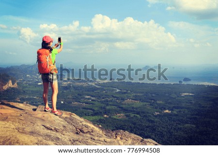 successful woman hiker taking picture with smartphone at cliff edge on mountain top
