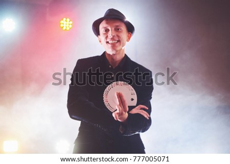 Magician showing trick with playing cards. Magic or dexterity, circus, gambling. Prestidigitator in dark room with fog.