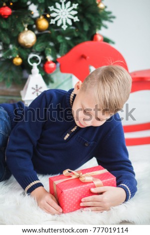 Closeup portrait of cute smiling teenage boy of 10 year old with present box sitting near Christmas tree. Vertical color photography.