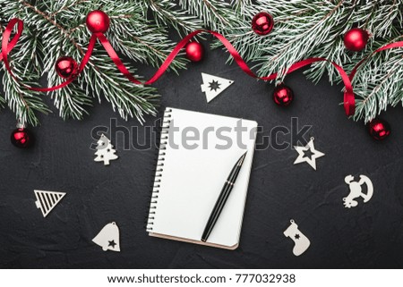 Notepad and pen, with space for text, wish decorated with fir branches, tree red globes, ribbon and handmade snowflakes toys on black stone background, view from top, above, Xmas greeting card 