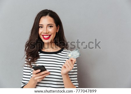 Portrait of a happy girl holding mobile phone and a credit card isolated over gray background