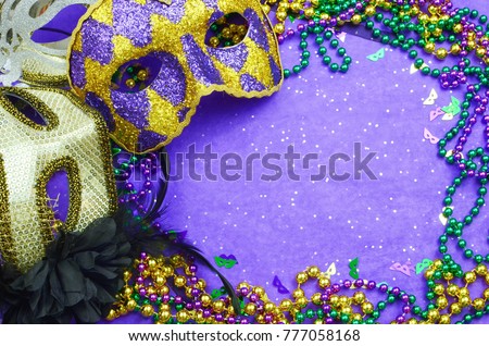 Mardi Gras border or frame of carnival masks, beads, ribbons and confetti in purple, green, gold and black on background of rough textured sparkly paper