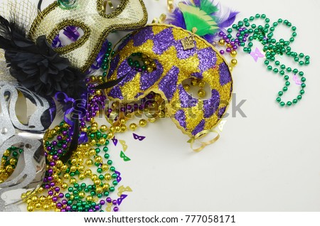 Mardi Gras border or frame of carnival masks, beads, ribbons and confetti in purple, green, gold and black on light background. Copy space