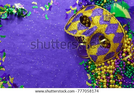 Mardi Gras border or frame of carnival masks, beads, ribbons and confetti in purple, green, gold and black on background of rough textured sparkly paper Royalty-Free Stock Photo #777058174