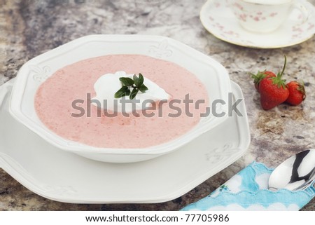 A bowl of chilled strawberry soup, garnished with a dollop of whipped cream and a fresh sprig of chocolate mint.