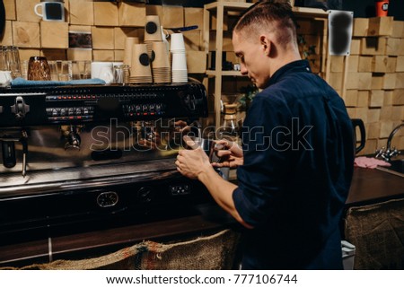Art work. Tasty drinks. Cropped image of handsome barista in apron holding a cup of coffee and working at the bar counter in cafe. Retro picture with little noise. 
