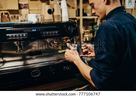 Barista preparing coffee beans drink. Cropped image of handsome barista in apron holding a cup of coffee. Retro picture with little noise and similaf focus