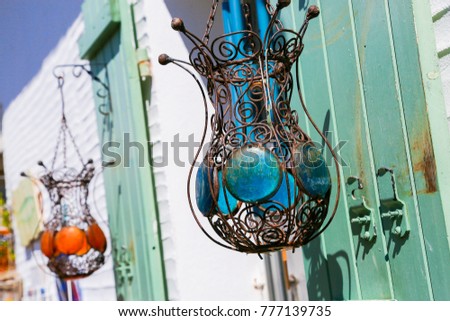 Two lamps made of wire filigree hanging from green shutters outside a white building. 