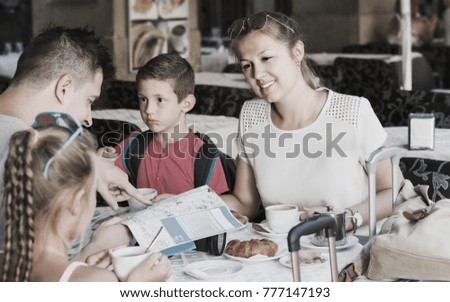 Husband with wife and children are resting in cafe and searching sights on map for visiting.