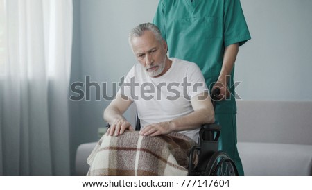 Disabled senior man sitting in wheelchair, male nurse supporting patient