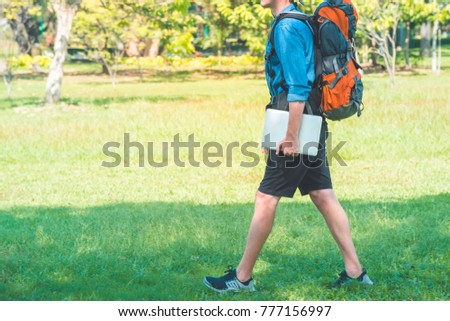 Man with a backpack walking in a park. Backpacker holding a laptop. Digital nomad concept