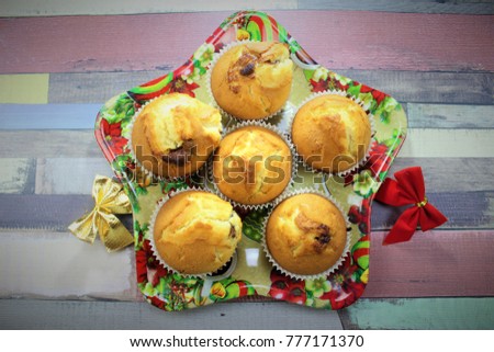 hot from the oven muffins filled with milka chocolate bar on the christmas plate in the shape of star with two christmas decorations on the side on the colored wooden table