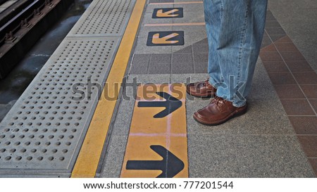 A man standing behind the yellow line for safety at city train station. 