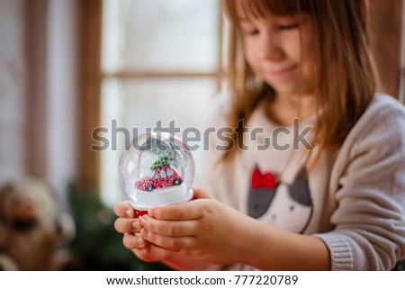 Happy little girl holding glass ball in room with holidays decorations