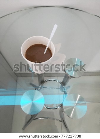 A cup of white coffee is placed on a clear glass table.