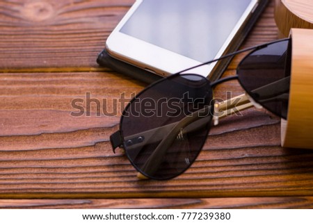 Tourist items on a rustic wooden table- black aviator sunglasses and moble phone, close up