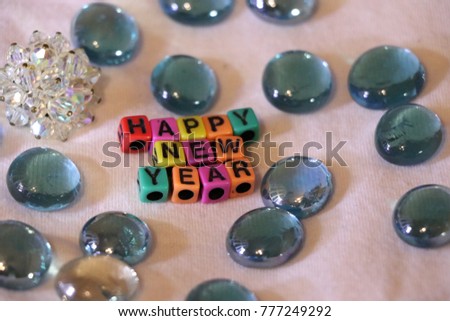 Happy New Year words and letters spelled with colorful alphabet bead blocks with clear blue glass pieces.