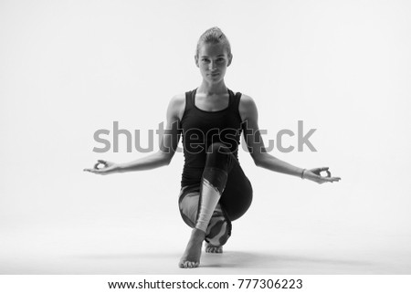 beautiful young girl sitting in yoga pose with legs crossed, holds balance, looks at camera, black and white photo
