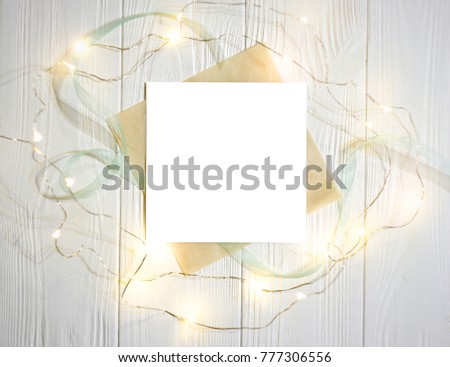 Festive light wooden background with frame of garland and white sheet.  Background for Christmas, New Year, birthdays greetings or any textual information.