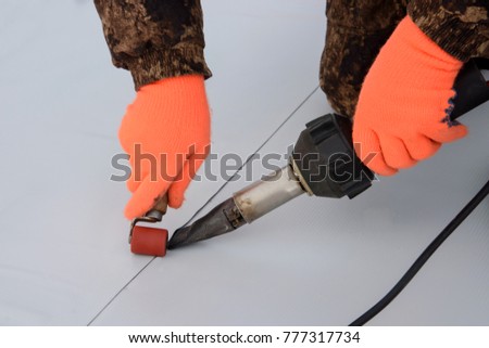 Waterproofing and insulation at construction site, roof sealing process of synthetic membrane with Hot Air Hand Tool. New protection technology. Closeup. Royalty-Free Stock Photo #777317734