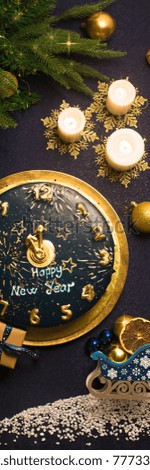 New year blue cake with golden clock hands showing midnight new year arrangement decoration, gift boxes, pine tree, candles dark blue table cloth sleigh of  chtistmas decoration ornaments, copy space