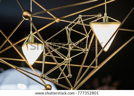 Modern chandelier in the form of a triangle and metallic geometric shapes, on a black background.