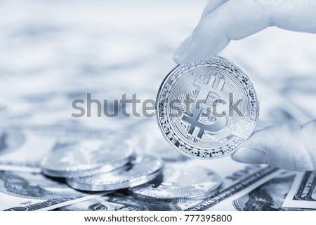 Bitcoin in female hand on dollar banknotes background, closeup. Blue tone. Digital currency