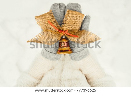 Christmas, New Year concept. Female hand in a white knitted mittens holding bell on winter background for Christmas. Free space.