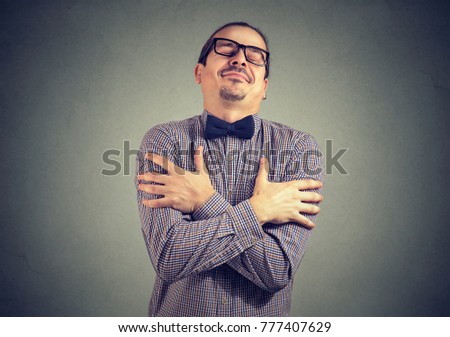 Young stylish man in bow-tie and eyeglasses embracing himself with great feeling of love.  Royalty-Free Stock Photo #777407629