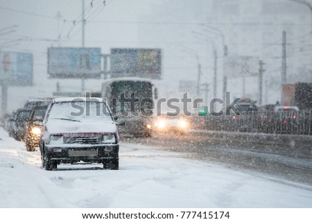 View of the street and parked cars during a snowfall/ heavy snow outside the city/ Extreme snowstorm in the European city, blurred car and billboard on background/ Bad weather, season, city concept