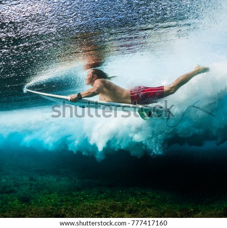 Young surfer dives under the ocean wave with surf board and performs trick named in surfing as a Duck Dive