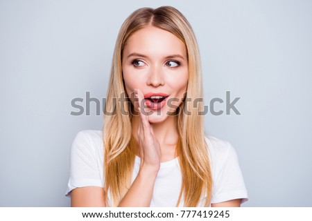 Don't tell anyone! Talkative mysterious pretty beautiful woman with blonde hair dressed in white tshirt is saying secret hot braking news and looking aside, isolated on grey background Royalty-Free Stock Photo #777419245