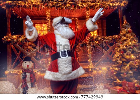 Cool modern Santa Claus in virtual reality glasses standing near his decorated house. Computer games. Christmas and New Year concept.
