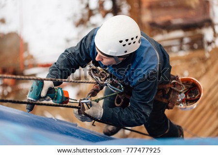 Professional industrial climber in helmet and uniform works at height. Risky extreme job. Industrial climbing at construction site Royalty-Free Stock Photo #777477925