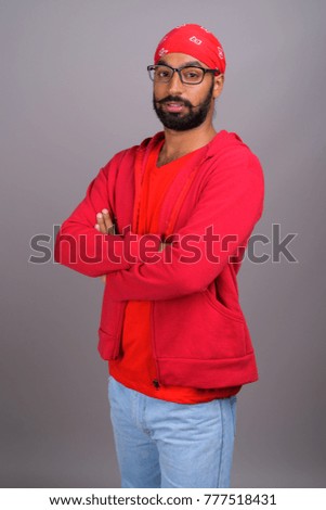 Studio shot of young handsome Indian man wearing eyeglasses against gray background
