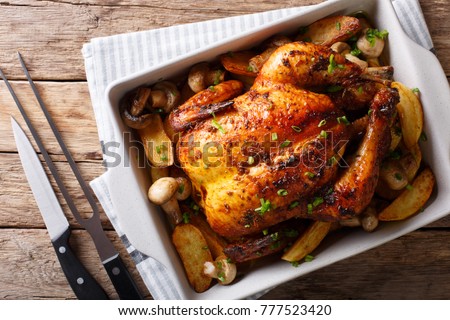 Whole baked chicken with mushrooms and potatoes close-up in a baking dish on a table. horizontal top view from above Royalty-Free Stock Photo #777523420