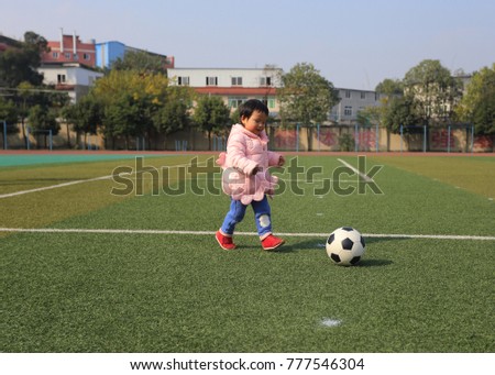 Cute girl playing soccer in the playground.The Chinese on the wall means "enhance physical constitution and improve quality"